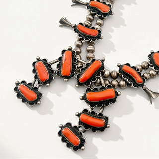 A Southwestern-style silver-toned beaded necklace featuring vibrant orange coral cabochons in ornate floral settings, displayed on a clean white background.