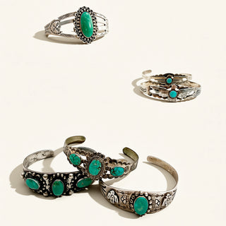 A set of silver-toned jewelry pieces with vibrant turquoise stones, including a ring and three cuff bracelets, arranged on a light cream background.