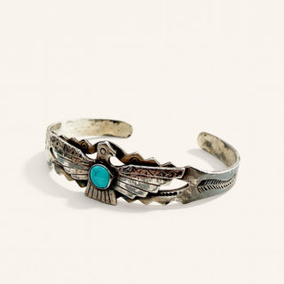 A sterling silver cuff bracelet featuring a detailed eagle design with a central turquoise stone, photographed on a clean off-white background.