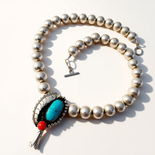 Silver beaded necklace with a turquoise and red stone pendant on a white background