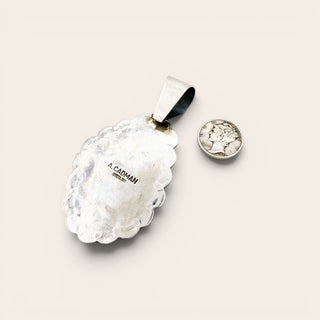 Silver pendant with 'A. Cadman' engraving on a light beige background