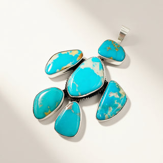 A silver pendant featuring seven polished turquoise stones of various shapes, arranged in a cluster on a light beige background.