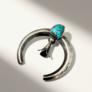 Silver crescent-shaped pendant with a turquoise stone on a white background