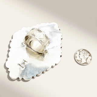Silver ring on a decorative silver dish with a coin for scale on a light background