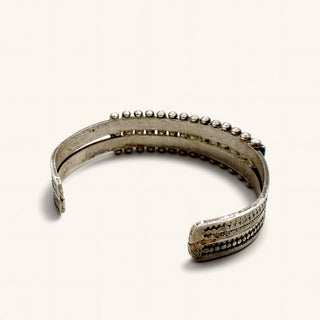 A silver-toned open cuff bracelet with textured geometric patterns and rows of small bead-like details along the top, photographed on a plain light background.