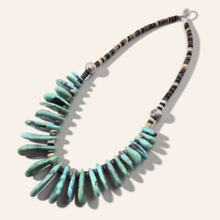 Turquoise beaded necklace with black and white accents on a white background