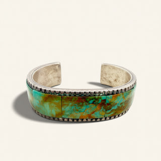 A silver cuff bracelet featuring a vibrant turquoise and green stone inlay, photographed on a clean off-white background.