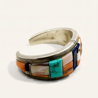A Southwestern-style cuff bracelet featuring a silver-tone metal band decorated with rectangular inlay stones in turquoise, orange, white, and dark blue.