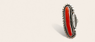 A Southwestern-style sterling silver ring featuring a large, polished red coral cabochon, set against a solid off-white background.