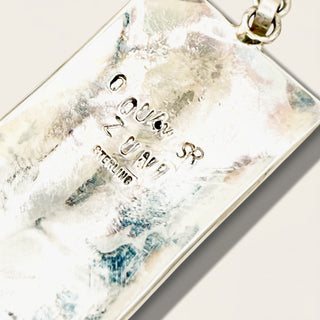 Close-up of a textured sterling silver pendant with  attached to a silver chain against a light beige background.
