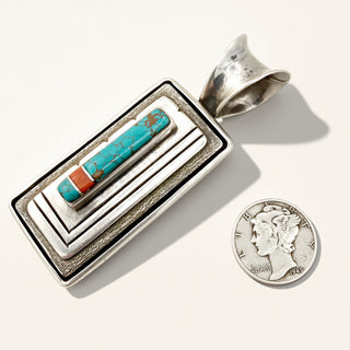 Silver pendant with turquoise and coral inlay next to a coin on a white background
