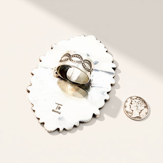 Silver ring on a decorative silver stand with a penny for scale on a white background