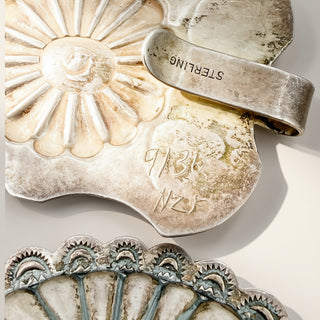 Sterling silver brooch featuring a sunburst flower design with a hinged tab and engraved details, shown on a light beige background.