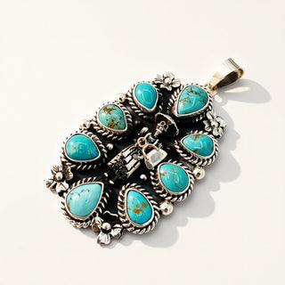 A sterling silver pendant featuring multiple turquoise stones in a Southwestern-style floral arrangement, photographed on a clean white background with soft shadows.