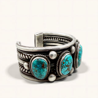 A wide sterling silver cuff bracelet featuring three oval turquoise stones with dark matrix, accented by small silver beads and twisted rope details, shown on a light off-white background.