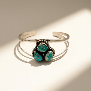 Silver cuff with three turquoise stones on a beige background