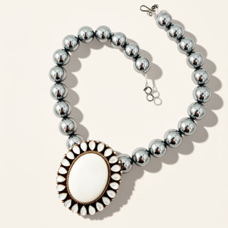 silver beaded necklace withy white stone on a beige background