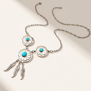Silver necklace with floral designs and turquoise stones on a beige background