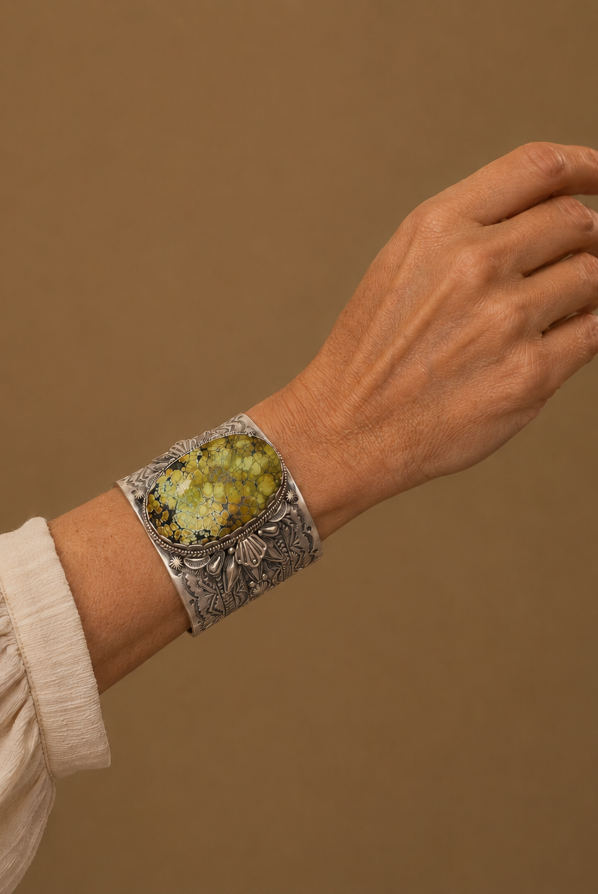 Hand wearing a silver bracelet with green gemstones against a brown background
