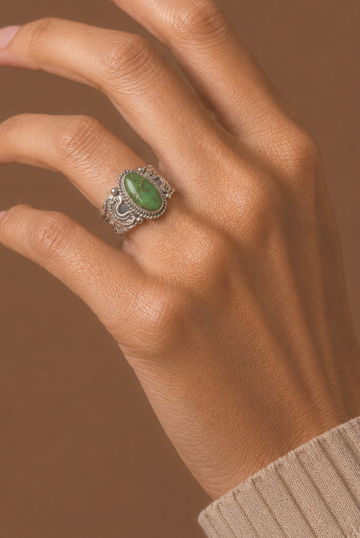 Hand wearing a silver ring with a green gemstone against a brown background
