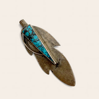 A vintage-style feather pendant or brooch featuring a textured brown metal base with a vibrant turquoise stone inlay, set against a plain off-white background.