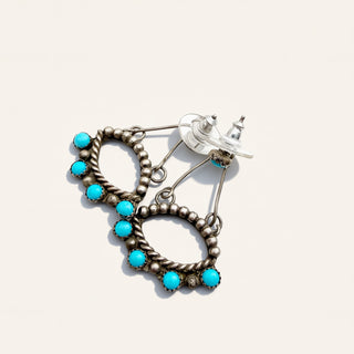 A pair of silver-toned dangle earrings with turquoise blue stones, displayed on a light beige background.