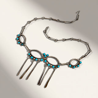 A silver-toned Southwestern-style necklace featuring turquoise blue stones and dangling bar charms, displayed on a neutral light gray background.