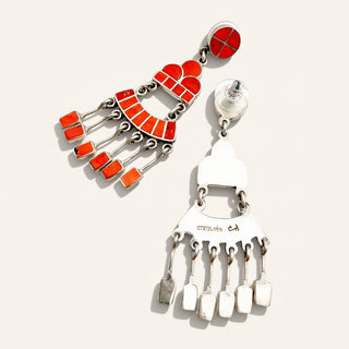 A pair of silver-toned statement earrings with vibrant red and orange enamel details, displayed on a light beige background.