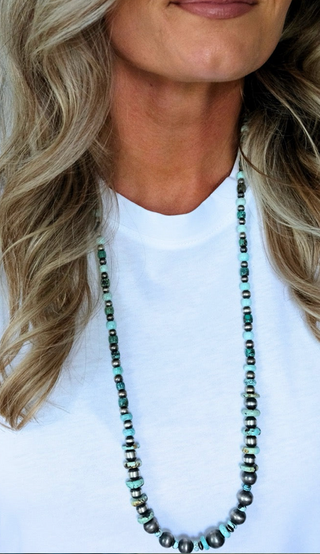 Person wearing a long beaded necklace with a plain background