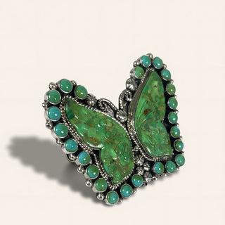 Butterfly-shaped green stone brooch with silver detailing on a beige background